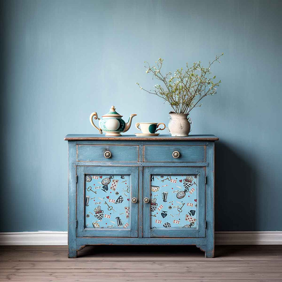Distressed blue cabinet with teapot display and Wonderland Whimsy decoupage on the lower doors, styled in a cozy vintage room.